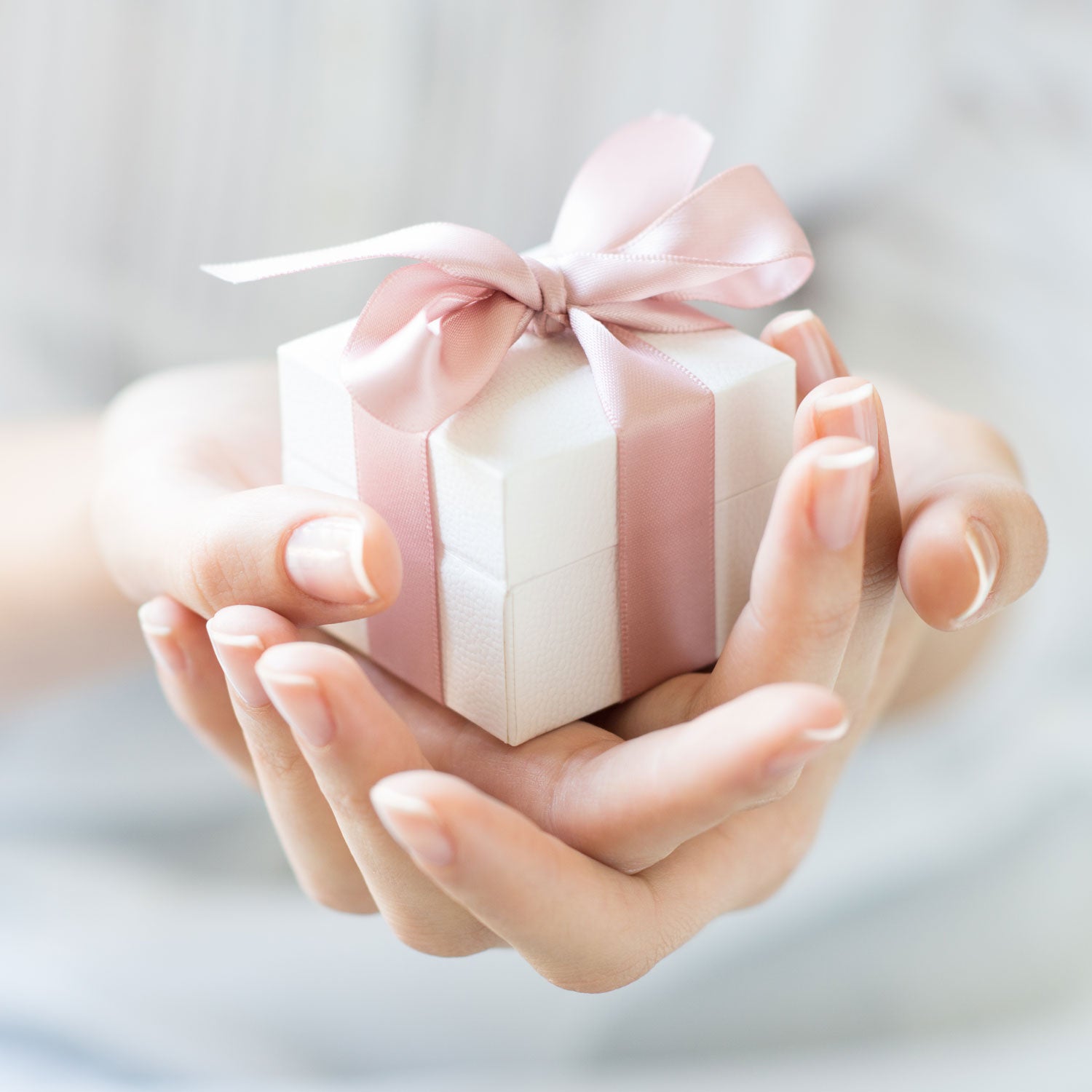 Foto eines Geschenks in zwei weiblichen Händen - Verapckung mit zartrosa Schleife